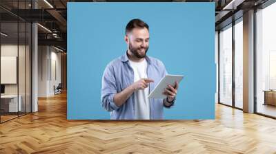 Joyful bearded man using tablet computer for online work or studies on blue studio background Wall mural