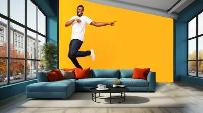 Joyful black guy jumping up and pointing aside Wall mural