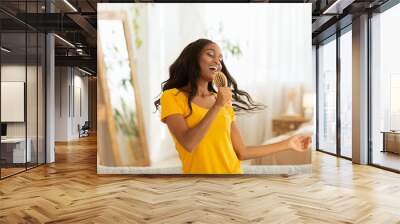 Joyful black lady with hairbrush as microphone singing and dancing at home Wall mural