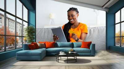 Joyful black woman making online payment, buying goods on web, using tablet and credit card at home. Internet shopping Wall mural