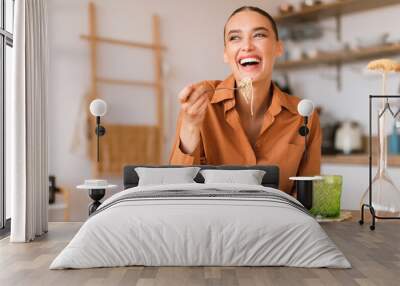 Kitchen happenings. Excited woman eating tasty homemade pasta, sitting in cozy kitchen interior, free space Wall mural