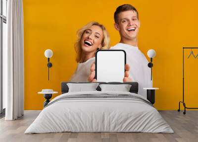 Laughing happy young caucasian male and female with open mouth show smartphone with empty screen Wall mural