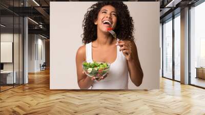 Laughing woman eating healthy salad over light background Wall mural