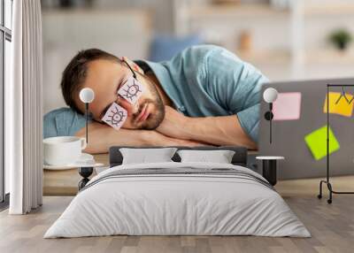 Lazy unproductive young guy wearing funny sticky notes with open eyes on his glasses, sleeping at workplace Wall mural