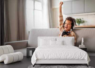 Little black boy in headphones holding joystick and raising hand in victory Wall mural