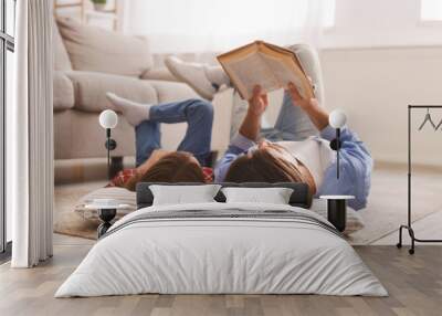 Little girl and father enjoying book together, laying on floor Wall mural