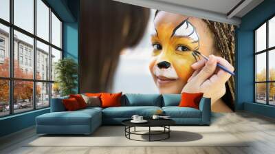 Little girl getting her face painted by face painting artist. Wall mural