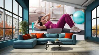 Lockdown sports. Sporty girl doing abs exercises to online workout video at home Wall mural