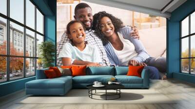 Loving afro family cuddling and smiling to camera at home Wall mural