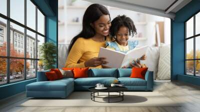 Loving black mom reading book to her cute little daughter at home Wall mural