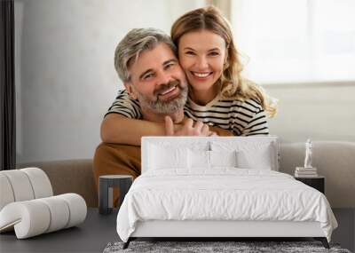 Loving Middle Aged Couple Embracing Sitting On Sofa At Home Wall mural