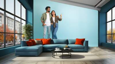 Loving young eastern couple pointing at copy space, colored background Wall mural