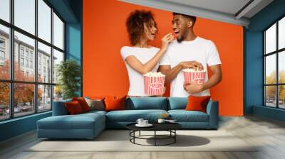 Man and woman eating popcorn on orange background Wall mural