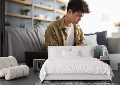 Man holding paper, writing and working on laptop at home Wall mural