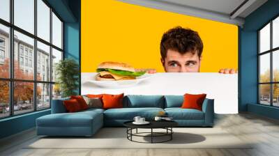 man peeking at tempting cheeseburger on plate against yellow background Wall mural