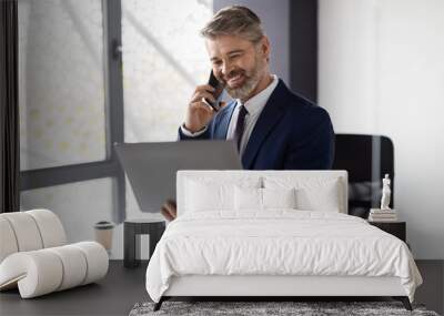 Mature Male Entrepreneur Talking On Mobile Phone And Using Laptop In Office Wall mural