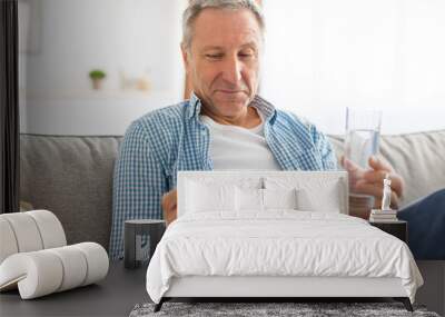 Mature man taking pills holding glass of water Wall mural