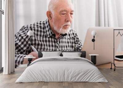 Mature man using laptop and writing in notepad Wall mural