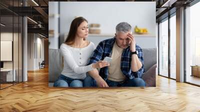 Mature woman confronting her husband about correspondence with his lover on smartphone Wall mural