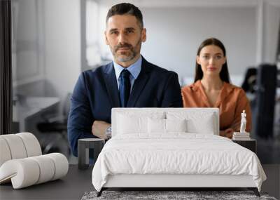 Middle aged businessman and young businesswoman with arms crossed posing in office and looking at camera Wall mural