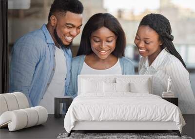 millennial afro girl showing funny content on smartphone to friends Wall mural