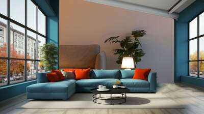 Modern sofa, glowing lamp on table in evening, plant in pot on floor on gray wall background in living room Wall mural