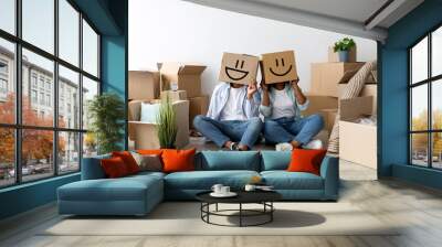 Moving and real estate concept. Black couple with cardboard boxes with smiley faces on head, sitting on floor Wall mural