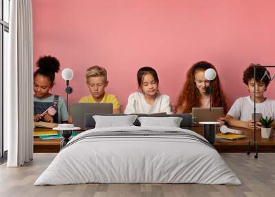 Multiethnic children with electronic devices and books studying at table over pink background, free space Wall mural