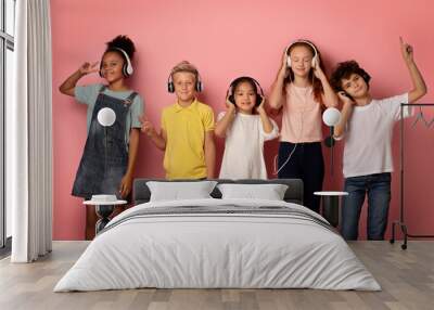 Multinational pupils in headsets enjoying music or listening to audio books over pink background Wall mural