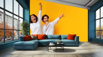 Multiracial couple dancing and singing together, having fun over yellow background Wall mural