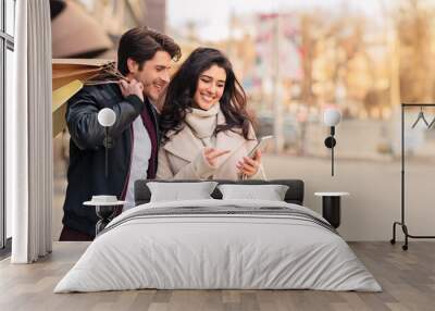 Order taxi online. Couple using smartphone after shopping in modern boutiques outdoors Wall mural