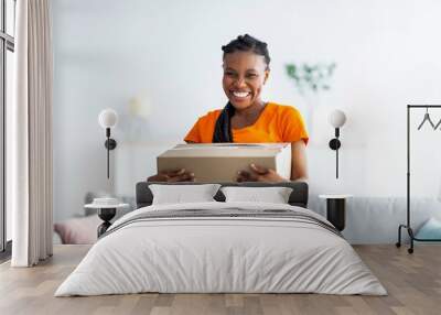 Overjoyed black lady holding cardboard parcel, receiving desired delivery, getting her online order at home Wall mural