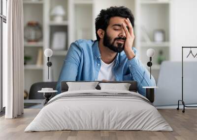 Overworked tired indian male entrepreneur sitting at desk in home office Wall mural