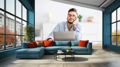 Overworked young freelancer man sitting at workplace and sleeping, napping while working on laptop, copy space Wall mural