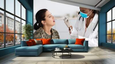 PCR Coronavirus Test. Black Doctor Lady Taking Swab From Female Soldier's Mouth Wall mural