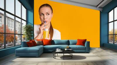 Pensive millennial girl drinking fresh orange vitamin juice with straw Wall mural