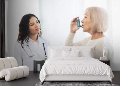 Physician examining mature woman using blue asthma inhaler Wall mural