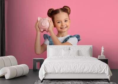 Portrait Of Cute Little Girl Holding Piggybank And Smiling At Camera Wall mural