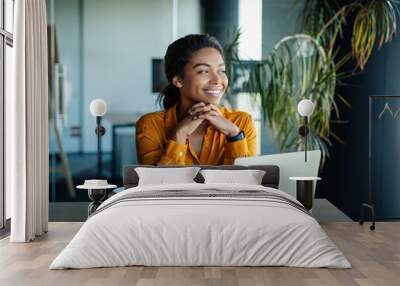 Portrait of dreamy african american businesswoman sitting at desk in office and thinking while working on laptop Wall mural