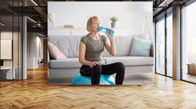 Portrait of fit mature woman drinking water from sports bottle on fitness ball indoors, free space Wall mural