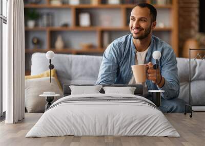 Portrait of handsome african american man resting on couch with cup of coffee Wall mural