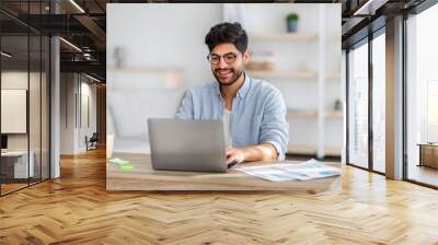 portrait of happy arab freelancer man sitting at desk with laptop computer at home office, looking a Wall mural