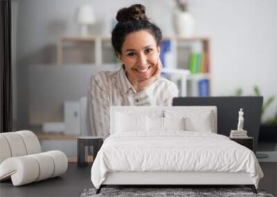 Portrait of happy businesswoman sitting at her workplace in front of laptop and smiling at camera at modern office Wall mural