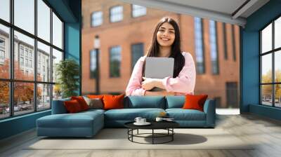 Portrait of happy hispanic lady student posing with laptop in hands outdoors, looking and smiling at camera Wall mural