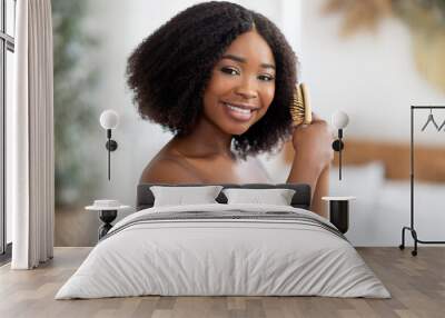 Portrait of happy young black lady brushing her curly dark hair at home Wall mural