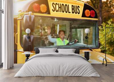 Portrait of joyful young black female driver steering yellow school bus Wall mural