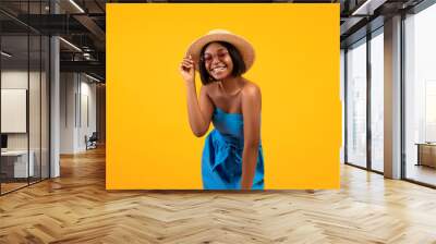 Portrait of lovely African American woman in beautiful dress, straw hat and sunglasses on orange studio background Wall mural