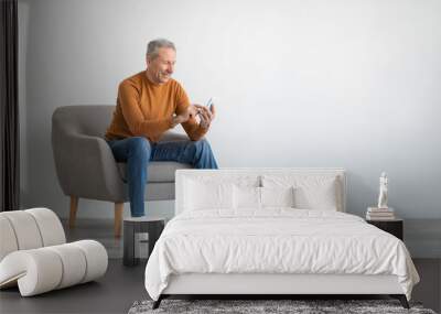 Portrait of mature man using smartphone sitting on armchair Wall mural