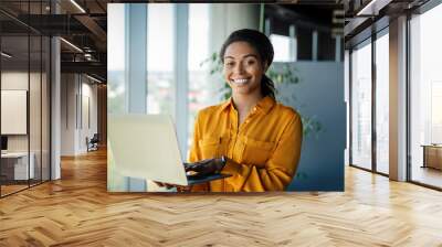 Portrait of positive black female entrepreneur standing near window and using laptop computer, free space Wall mural