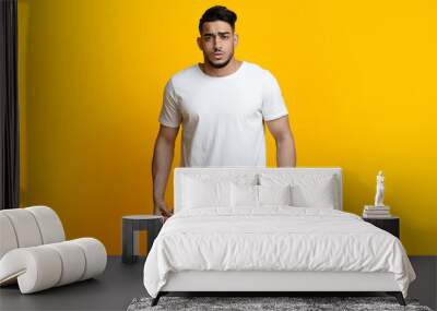 Portrait of sad man showing empty pockets on yellow background Wall mural